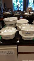 Photo showing six baking dishes including Corning Ware Blue Cornflower pattern dishes with glass lids, and nested plain white bowls.
