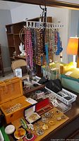 Beaded necklaces hanging on a rack with assorted jewelry boxes and pins displayed on a table.