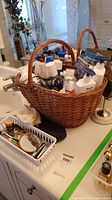 Basket filled with various personal care bottles, hairdryer visible, and grooming items in a white container on a table