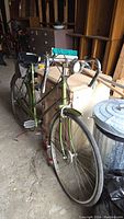 Full view of green Raleigh bicycle showing frame, wheels, fenders, chain guard, headlight, saddle bag and pump
