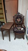 Vintage needlepoint upholstered armchair with carved wooden frame next to rectangular wooden side table.