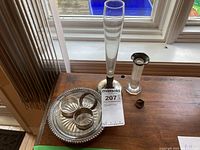 Lot arranged on wooden table by window showing all items: round dish with three napkin rings, glass vase with silver base, and silver candle holder.