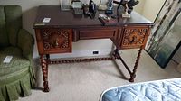 Front view of vintage wooden desk with ornate carved drawer fronts and spiral turned legs.