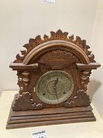 Front view of vintage mantel clock showing carved wooden case and metal clock face with keyholes and Arabic numerals.