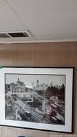 Framed photograph hanging on a wall with visible ceiling vent above, showing vintage Ottawa city scene with streetcars and buildings.