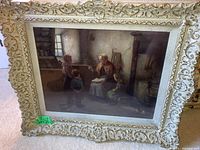 Full view of vintage framed print showing an elderly woman teaching three children in a rustic interior, the frame is detailed and carved with an off-white finish.