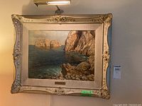 Full view of ornate framed coastal rock print with light fixture above and green measurement sticker