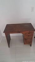 View of small antique wooden desk showing rectangular top, worn dark brown finish, right side drawers and cabinet door