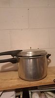 Side angle view of a metallic stove top pressure cooker with black handles on a wooden surface.