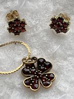 Overview of red gemstone pendant on chain with matching stud earrings on white backdrop