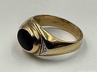 Front angle view showing oval black onyx cabochon and triangular diamond accent. Interior “10K” stamp visible.