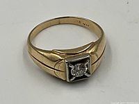 Top view showing round diamond solitaire in square white metal mount on yellow gold band