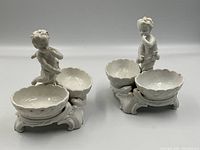 Front view of both figural salt cellars showing scalloped bowls and cherub figures