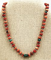 Front view of the antique necklace with coral and turquoise beads hung against a beige fabric background, showing the bead details and arrangement.