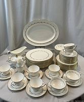 Wide view of entire dinnerware set arranged on table in front of grey curtain background.