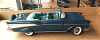 Side view of blue 1957 Chevrolet BelAir die-cast model car with convertible top down, showing whitewall tires, detailed interior, and chrome trim.