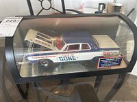 View of the model car in its display case showing the side profile and decals including 'COLOR ME GONE II' and '987'.