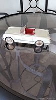 Side view of white die cast Chevrolet convertible model car with red interior on glass table, showing front wheel friction drive.