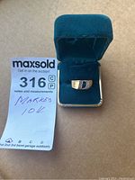Ring displayed in open blue velvet case alongside auction tag showing purity marking