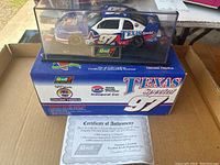 Side and top view of the Interstate Batteries Texas Special #97 diecast model car inside clear plastic display case with Revell Collection plaque and original retail box below.