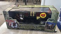 Front and side views of The Munsters Koach die-cast model in original box with packaging graphics and branding visible.
