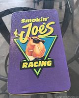 Purple metal tin with 'Smokin' Joe's Racing' logo featuring a cartoon camel wearing sunglasses and smoking a cigarette
