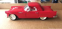 Side view of the 1955 Ford Thunderbird die-cast model car in red, showing closed doors and fixed hardtop roof.