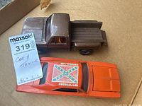 Image showing both model cars, the brown Chevrolet Stepside truck and orange General Lee car with visible Confederate flag decal on roof.