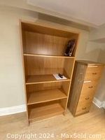 Photo showing a light brown wooden Ikea bookcase with four shelves partially filled with a book and a notebook, next to a matching 4-drawer filing cabinet.