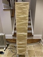 Front view of the beige textured paper floor lamp showing its tall rectangular shape and fold lines on the paper shade.