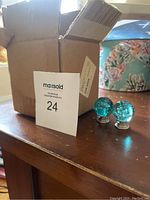 Two blue glass cabinet knobs with silver bases displayed on a wooden surface next to a cardboard box.