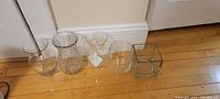 Four clear glass vases displayed side by side on a hardwood floor.