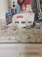Photo of four Marvel Avengers shot glasses on countertop, along with the Marvel Avengers branded box packaging behind them.