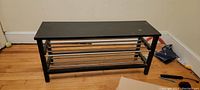 Photo showing a top-down view of the rectangular black wooden bench with metal shoe racks.