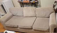 Front angled view of the grey three-seater sofa showing three seat cushions and back cushions, armrests, and general fabric condition.
