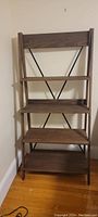 Full view of wooden tiered ladder bookshelf showing all five shelves, metal X-shaped back braces, wood grain, and overall structure.