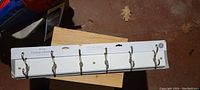 Photo of white wooden coat hanger hookrail with six metal double hooks displayed flat on surface.