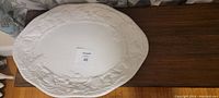 Top-down view of an oval white ceramic platter with embossed grapevine pattern on the edges, showcasing the size and decorative details.