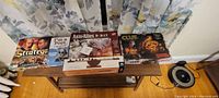 Five games displayed on a wooden table including Strategy Classic, I'm a Poet, Axis & Allies D-Day, Clue and a small Roach Archimedes card game.