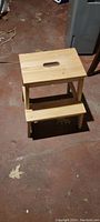 Top view of the two-step wooden stepping stool on a concrete floor.