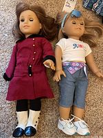 Front view of both dolls side by side on carpet; showing outfits and overall condition.