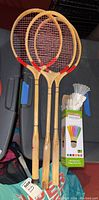 Three wooden badminton rackets standing upright with a box of LED shuttlecocks next to them on a black surface.