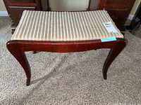 Full side view of the wooden bench showing curved legs and striped worn upholstered seat