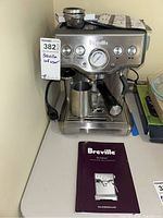 Front view of stainless steel Breville Infuser espresso machine with portafilter attached and milk frothing pitcher underneath