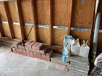 Red bricks stacked with gray concrete pavers and bags placed beside them inside a garage.