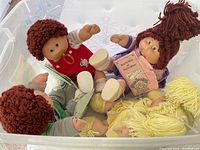 Four Cabbage Patch Kids dolls in a box with visible certificates, showing yarn hair and various outfits.