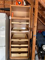 Full view of the tall wooden cabinet with open pull-out shelves and open top shelf. Cabinet positioned in garage among other items.