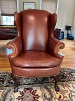 Front view of brown leather Hancock & Moore armchair showing nailhead trim and carved wooden legs on Persian style rug.