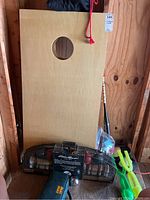 Wooden cornhole board with hole and croquet set basket, baseball bat, green snowball makers.
