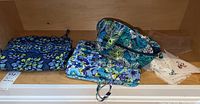 Two Vera Bradley bags with floral patterns and a stack of white handkerchiefs.